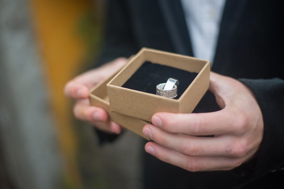 A silver ring elegantly presented in a gift box held by a person outdoors, suggesting a special occasion.