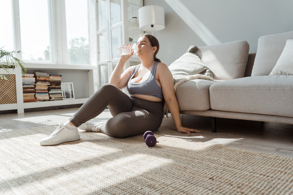 A woman in activewear relaxes at home with a drink after exercising, embodying fitness and self-care.