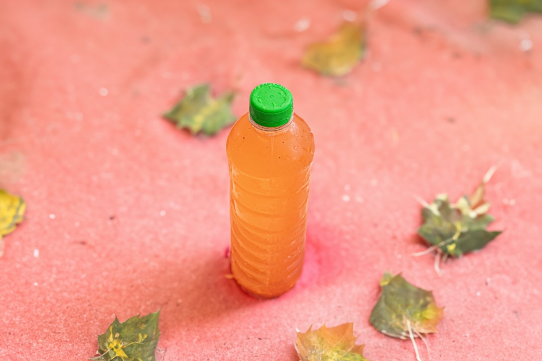 A bottle of orange liquid sitting on a pink surface