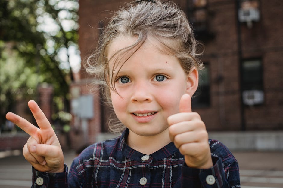 Happy child outdoors showing peace sign and thumbs up with a smile.