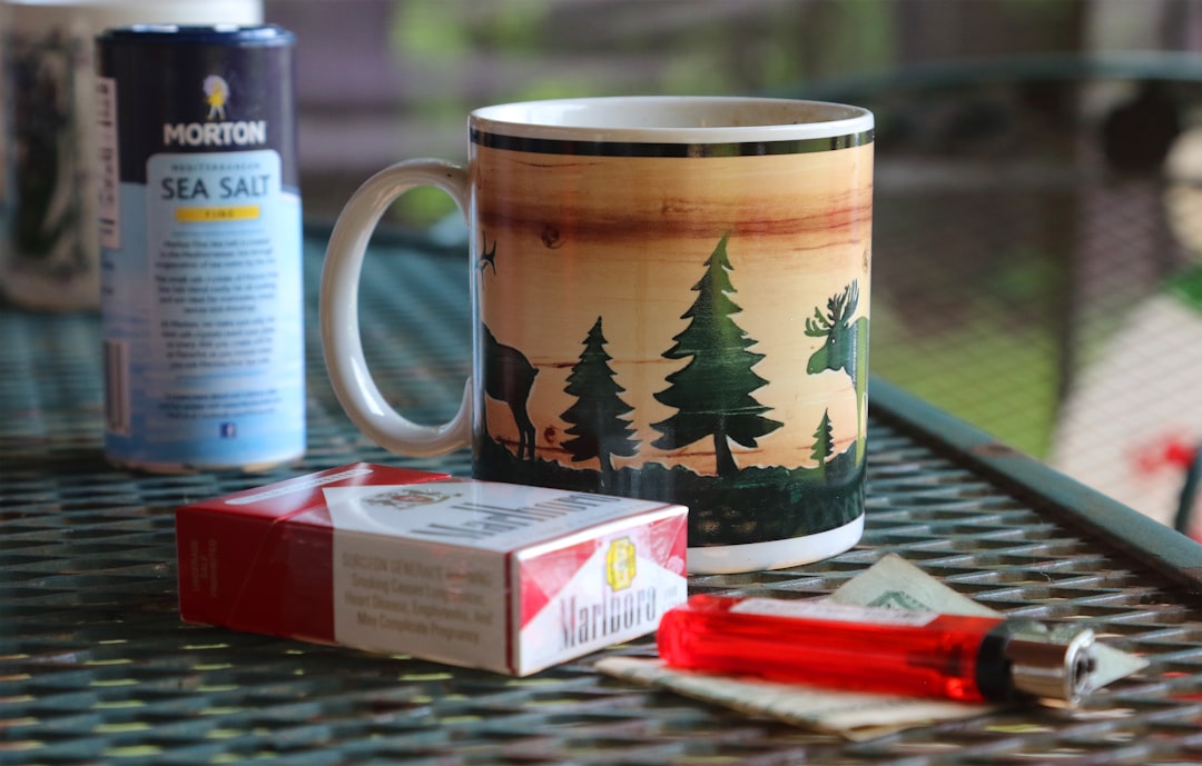 a coffee mug sitting on top of a table next to a box of cigarettes