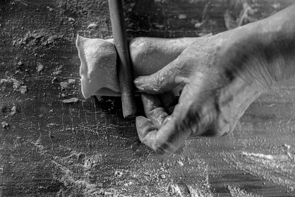 Monochrome image of hands rolling dough with a pin on a flour-dusted surface.