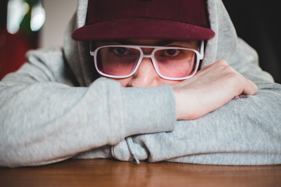 A young man in a hoodie and glasses looks pensively at the camera, offering a contemplative mood.