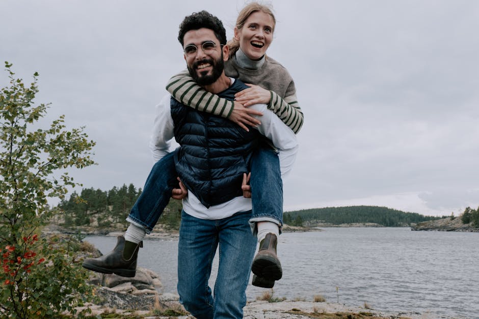Smiling couple enjoying a piggyback ride by a scenic lake. Outdoor adventure and joy.