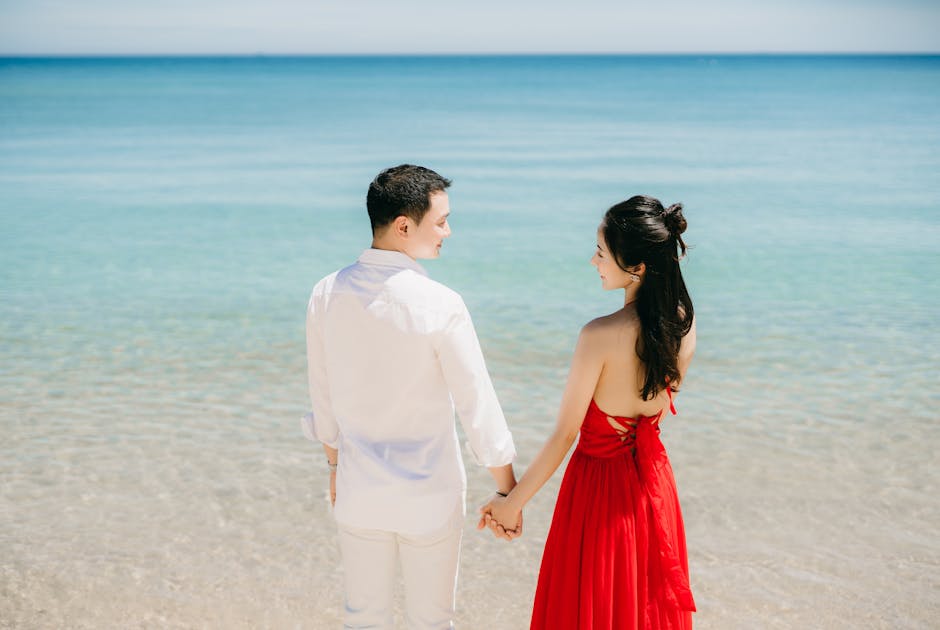 A couple holding hands and gazing at the serene sea on a sunny day.
