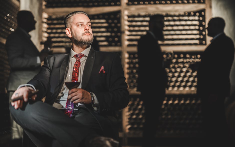 Elegant man in a suit enjoying a drink in a wine cellar, surrounded by shadows.