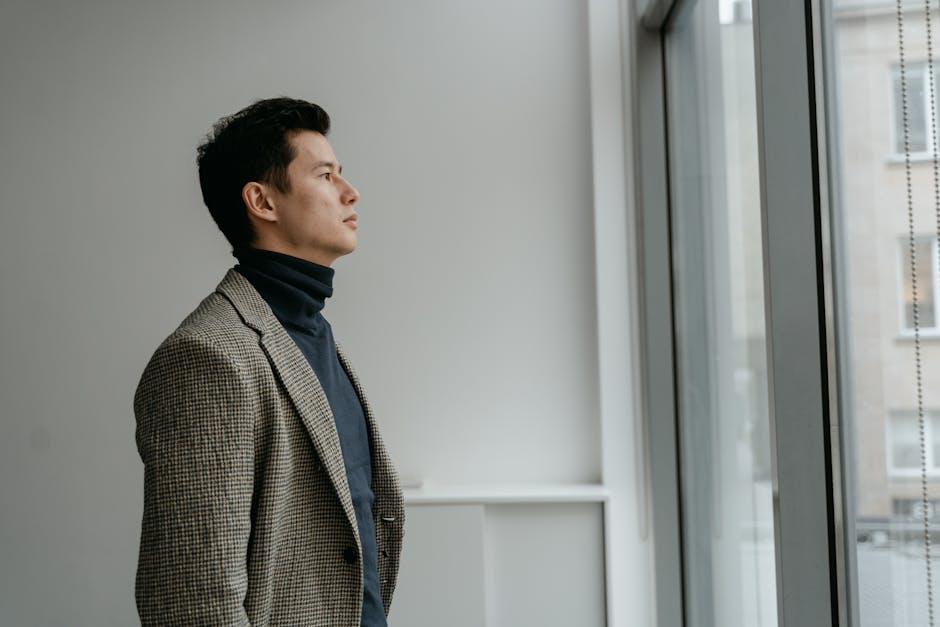 Portrait of a man in a turtleneck gazing through a glass window in a modern interior setting.