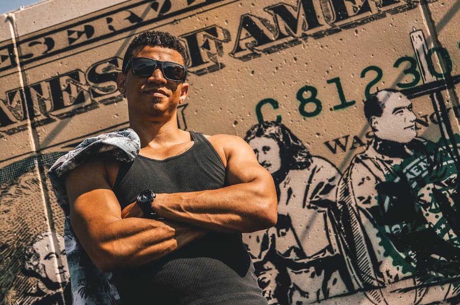 Stylish man with sunglasses posing confidently against a graffiti-covered wall in summer.