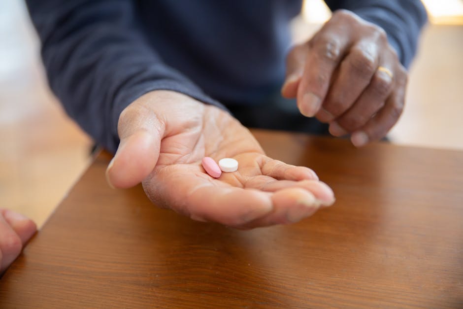 A close-up view of hands holding pink and white pills on a wooden table.
