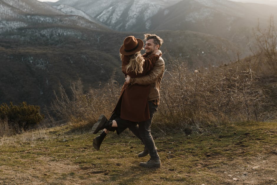 A joyful couple embraces outdoors, surrounded by breathtaking mountain views, showcasing natural romance.