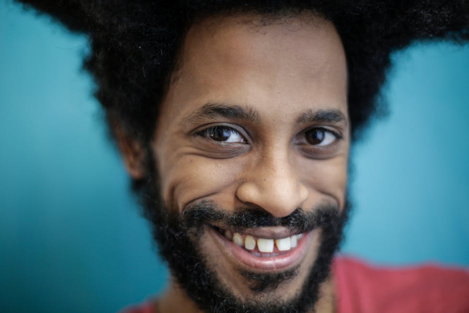 A vibrant close-up portrait of a smiling man with facial hair against a blue background.