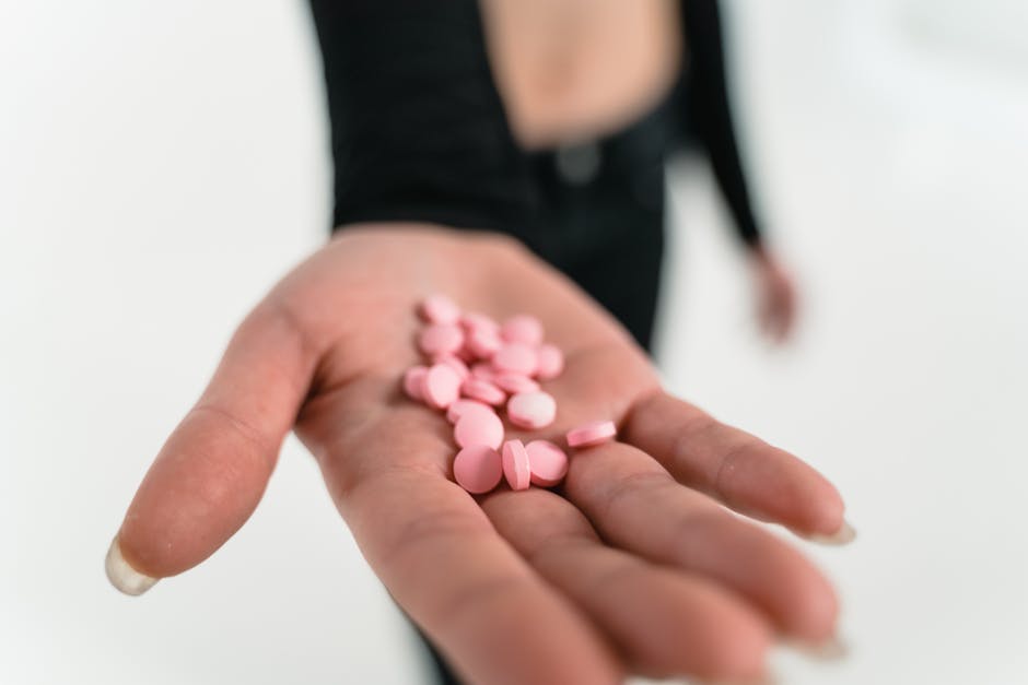Close-up image of a hand holding pink pills against a blurred background.