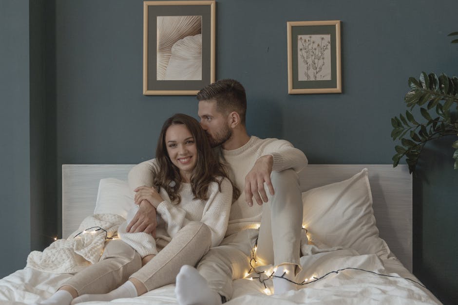 A loving couple enjoys a warm moment with string lights in a cozy bedroom setting.