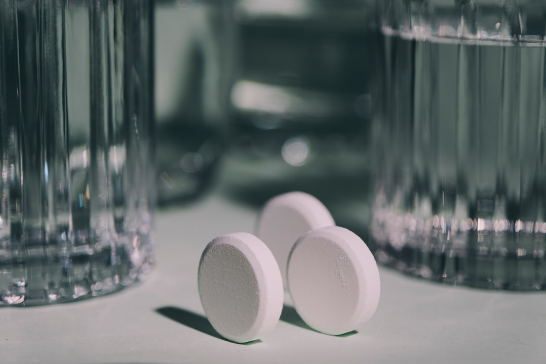 Three pills sitting on top of a table next to a glass of water