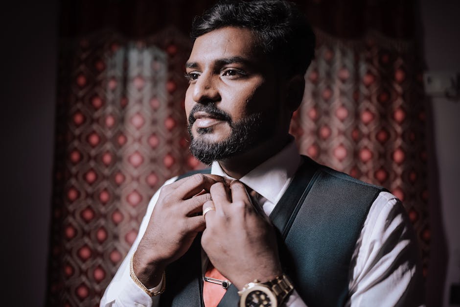 Portrait of an Indian groom adjusting his tie indoors before the wedding ceremony, exuding elegance and focus.